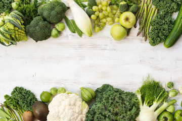 Green vegetables and fruits on the white wooden table, copy space for text in the middle, horizontal, top view, selective focus