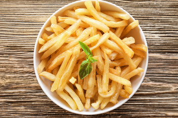 Bowl with yummy french fries on wooden table