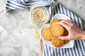 Woman taking oatmeal cookie from plate