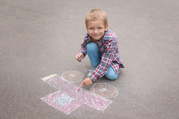 Naklejka premium Little boy drawing car with chalk on asphalt
