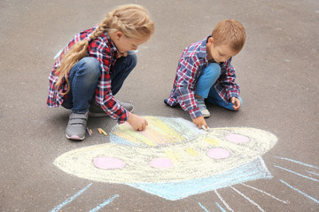Little children drawing alien spaceship with chalk on asphalt