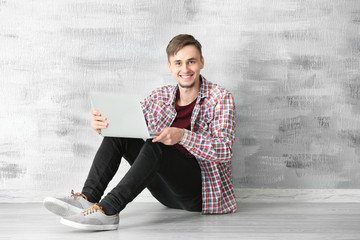 Young man with laptop sitting on floor near wall