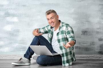 Handsome man with laptop sitting on floor near wall