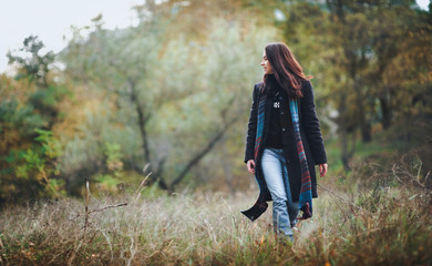 A pretty girl in a woolen coat with a long scarf walks through the autumn forest against the backdrop of nature.