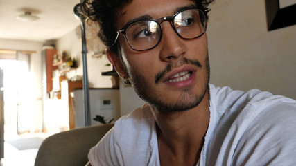 Handsome young man talking to the camera and smiling, at home in his living-room