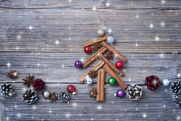 Christmas tree made from cinnamon sticks with decoration on rustic background. Snow effect, copy space, toned