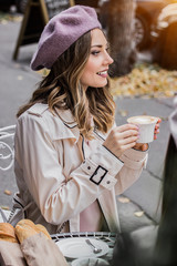 Moments of joy. Side view of beautiful young french woman in beret looking away and smiling while drinking coffee in french vintage cafe. Spending time with best friend. Women drinking coffee. - obrazy, fototapety, plakaty