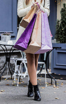 Walking with new purchases. Cropped image of young woman in coat holding shopping bags in hands while walking the city streets. Black friday shopping. Big sales concept.