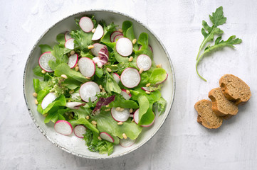 Vegan salad with radish, lettuce, arugula (rucola) and pine nuts on white background. Top view. 