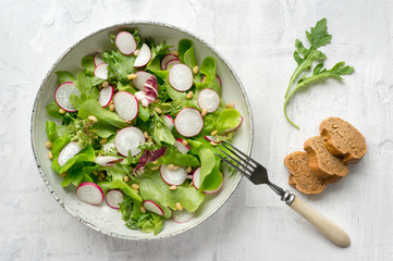 Vegan salad with radish, lettuce, arugula (rucola) and pine nuts on white background. Top view.