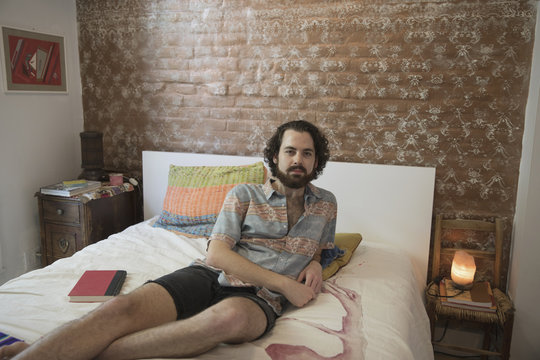 Portrait of young man leaning on bed at home