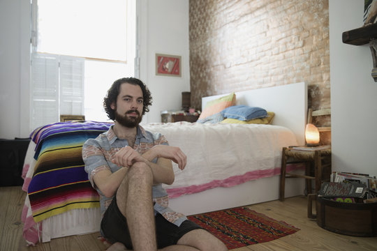 Portrait of young man sitting besides bed at home