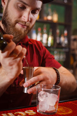 The barman pours whiskey into a glass with ice