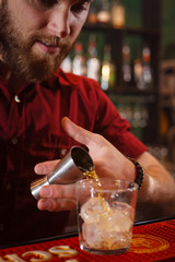 The barman pours whiskey into a glass with ice