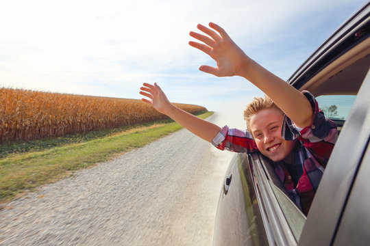 Boy Putting His Heads And Hands Out Of The Car Window Driving Down A Country Road