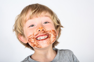 Young messy boy eating a chocolate bar with chocolate on his face