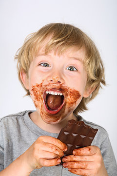 Young Messy Boy Eating A Chocolate Bar With Chocolate On His Face And Hands