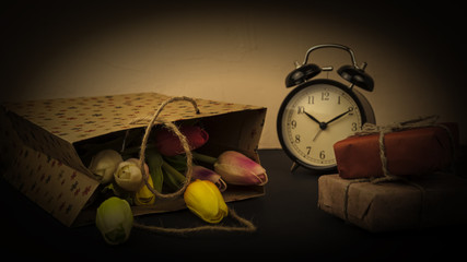 Multicolored flowers in festive packages and gifts and an alarm clock the concept of a holiday