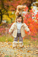 Little girl with a teddy bear in her hand on a background of autumn foliage. Autumn time.