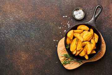 Roast potato with salt and spices in pan on wooden board on brown background with copy space. Top view.