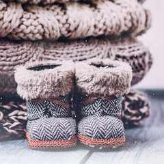 Stack Pile of Cozy Knitted Sweaters and Holiday Christmas Baby Toy Small Boots on a Wooden Table Background. Warm Cozy Concept. Snow, toning image