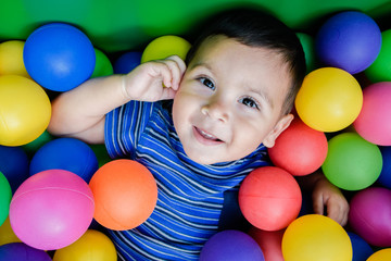 Fototapeta na wymiar Happy little boy playing in the pool with colorful plastic balls.
