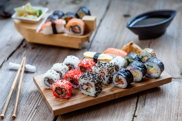 A variety of sushi on old wooden table. Sushi rolls, nigiri, raw salmon steak, rice, cream cheese, avocado, lime, pickled ginger.