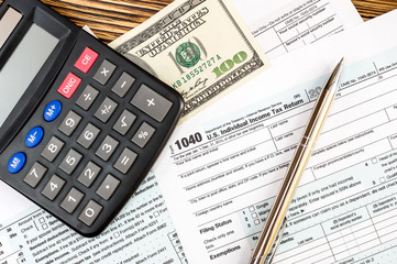 Calculator with one hundred dollar bill on the tax form. Top view.