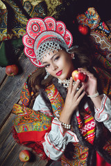 Girl in folk costume and headdress holding a red Apple in the style fashion on dark wooden background top view