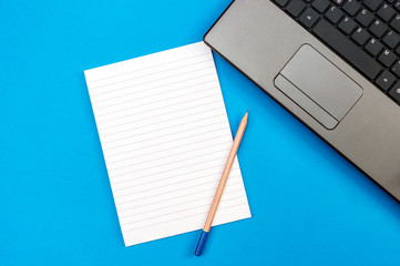 Open notepad with pencil and laptop on a blue. Top view. Business and education concept.