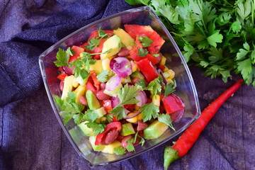 Mexican salad with tomato, avocado, red beans, corn, paprika, red onion, lemon, chili, olive oil, parsley