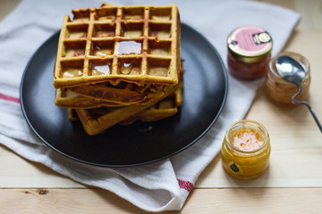 Freshly baked sweet delicious appetizing Belgian waffles made of pumpkin with honey on a black plate on a wooden table.