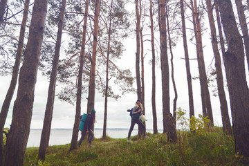 Obraz premium Girlfriends with backpacks walking through the forest in front of lake and forest view. A hipster traveler exploring the world.