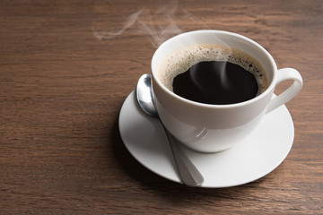 a hot coffe white cup on the wood table with small spoon and steam. Morning concept.