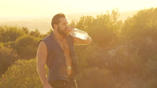 Portrait of strong man drinks and pours himself from bottle with water. Slowly