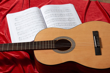 Fototapeta na wymiar acoustic guitar and music notes on red fabric, close view of objects