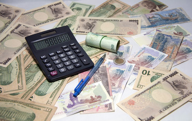 Black calculator and blue ballpoint pen with roll Thai banknotes use a rubber band on the various nations banknotes, Concept of business and finance.