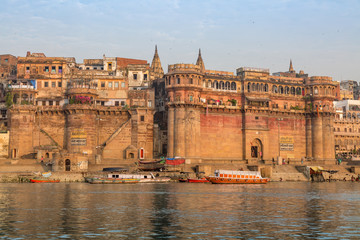 Historic Varanasi city with old architectural buildings and ancient temples along the Ganges river ghat as viewed from a boat.