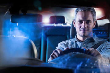 Front view. Gray haired man driving his car at night in the rain