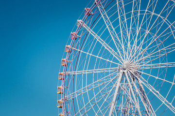 Close up part of colorful ferris wheel with blue sky background at public park in vintage style.