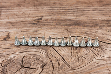 Row of screws with a drill head, stand on an old wooden surface.