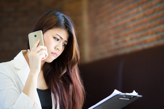 Asian working women age between 25-35 years old speking with cell phone and looking at a paper.