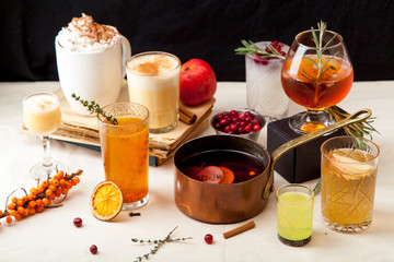 Set of various winter cocktails: mulled wine, eggnog, limoncello, old-fashioned, coconut margarita. Black background, white linen tablecloth.