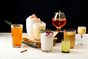 Set of various winter cocktails: mulled wine, eggnog, limoncello, old-fashioned, coconut margarita. Black background, white linen tablecloth.