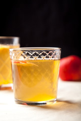 Two vintage glasses with apple cider on black background. Christmas beverages concept. Two red apples and rosemary sprig aside.  Warm backlight. Vertical composition.