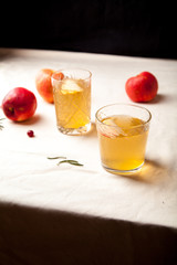 Two vintage glasses with apple cider on black background. Christmas beverages concept. Two red apples and rosemary sprig aside.  Warm backlight. Vertical composition.