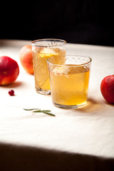 Two vintage glasses with apple cider on black background. Christmas beverages concept. Two red apples and rosemary sprig aside.  Warm backlight. Vertical composition.