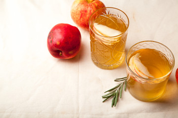 Two vintage glasses with apple cider on black background. Christmas beverages concept. Two red apples and rosemary sprig aside.  Warm backlight.