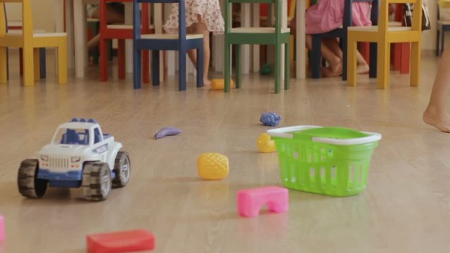 Children play at a kindergarten. Kids run at the playroom. Baby's legs and toys at playschool