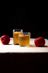 Two vintage glasses with apple cider on black background. Christmas beverages concept. Two red apples and rosemary sprig aside.  Warm backlight. Vertical composition.